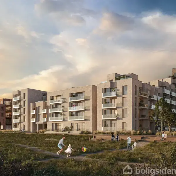 Moderne lejlighedsbygninger står ved siden af hinanden under en klar, blå himmel. Foran bygningerne leger folk omkring med en bold på et grønt, græsbeklædt område.