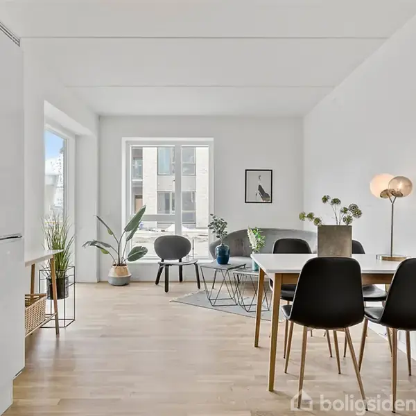 Et moderne spisestue-køkken med trægulv. Et spisebord med sorte stole og dekorative planter på bordet. Store vinduer lader lys strømme ind, omgivet af minimalistisk interiør.