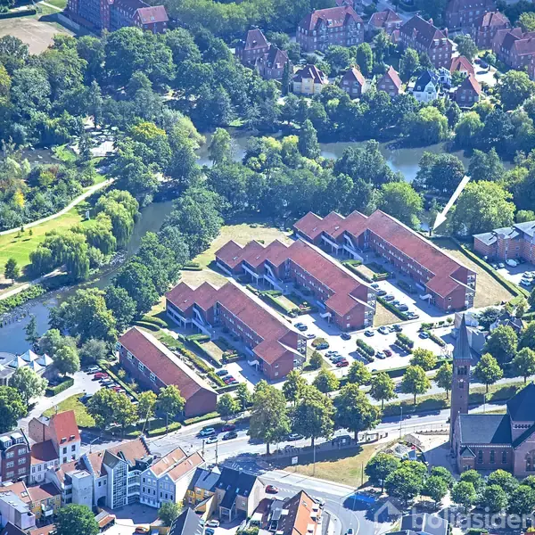 Luftfoto af en by med huse og veje, omgivet af grønne områder og en flod. Byens tæthed aftager mod horisonten, hvor landskabet bliver mere landligt.