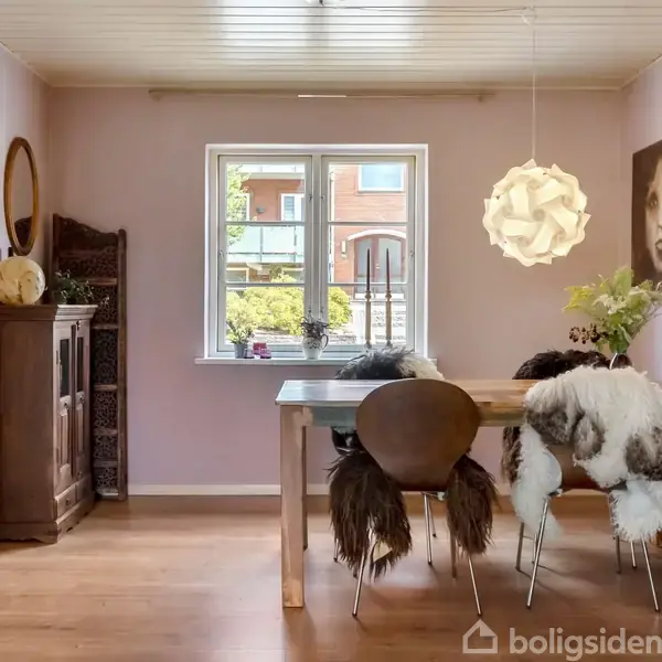 Spisebord med to stole dækket af pels, står i en lys spisestue. En kunstnerisk lampe hænger over bordet, omringet af en vase med blomster og et maleri på væggen.