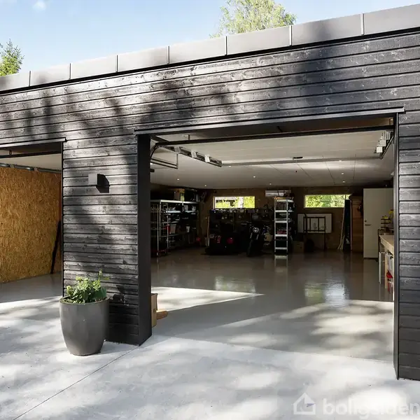 Sort trægarage med åbne porte viser organiseret interiør med hylder og værktøj. Sollys skinner ind, omgivet af træer. En enkelt plante står ved siden af indgangen.