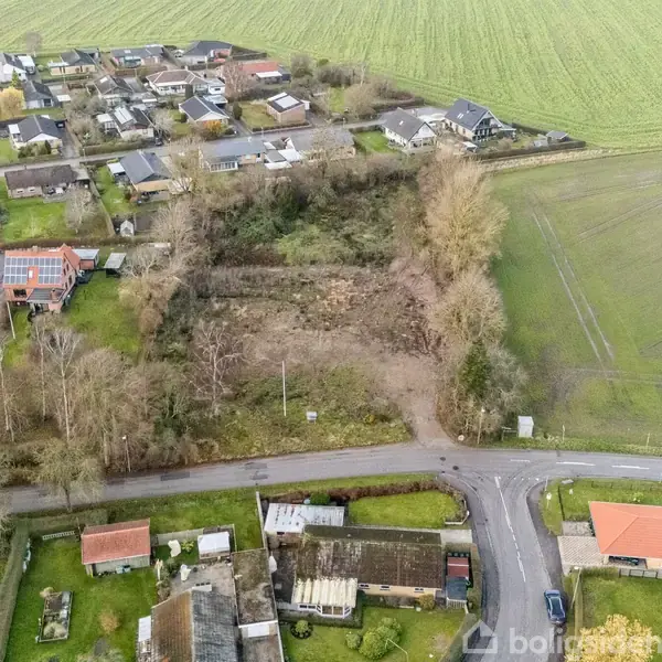 Et område med åbent landskab omkranser en bebyggelse med huse og haver. Veje krydser forbi, og marker strækker sig i baggrunden.