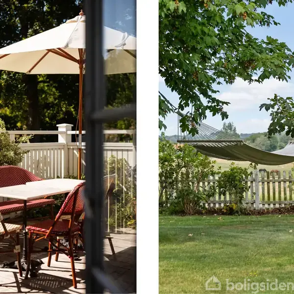 En terrasse med røde kurvemøbler og stort parasol; i baggrunden, en have med græsplæne og en hængekøje mellem to træer, omgivet af et hvidt stakit og grønne landskaber.