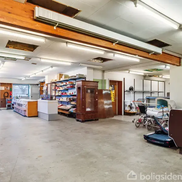 Butikken har åbne hylder med diverse varer og møbler; barnevogne står i midten, mens lyskilder hænger fra loftet og skaber et oplyst interiør. Døren i baggrunden leder ud.