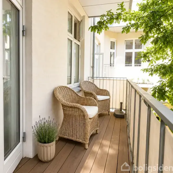 To fletstole med hvide hynder står på en balkon med trægulv. Rækværket er af metal, og en grøn plante ses i forgrunden.