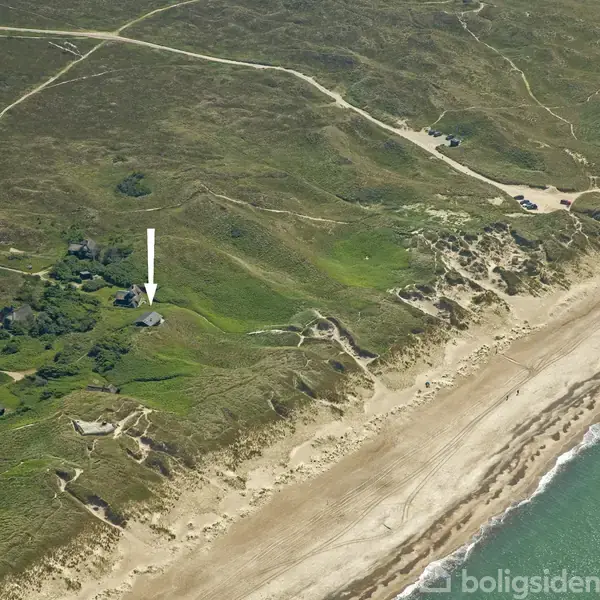 Kystlinje strækker sig langs venstre side med huse spredt i grønt landskab. En hvid pil peger på et specifikt område. Havet til venstre, marker og søer til højre.