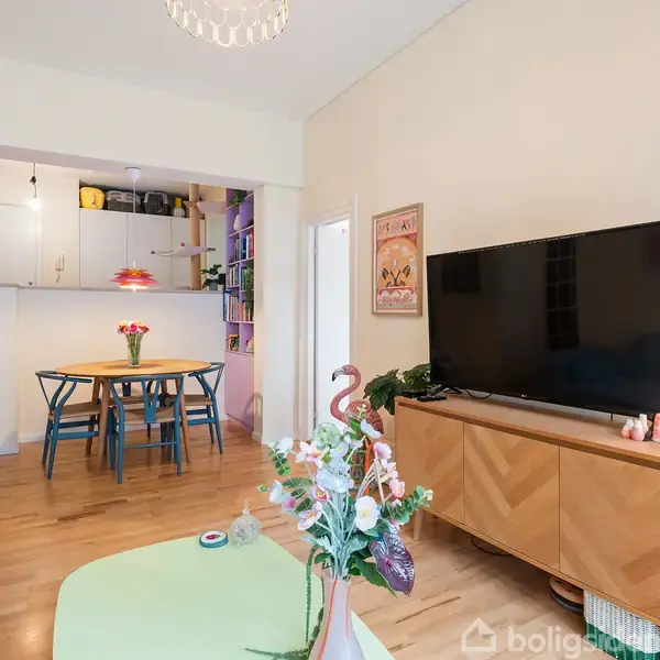 En stue med en stor fladskærms-tv på et skab. Et spisebord med seks blå stole står i en alrum. En buket blomster på et bord ved en lysegrøn sofa.