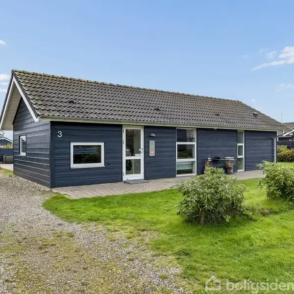 Et mørkeblå enfamiliehus med stor tag og hvidrammede vinduer står på en grusvej. Til venstre græsområde og busk. Nummer 3 på væggen. Blå himmel med få skyer.