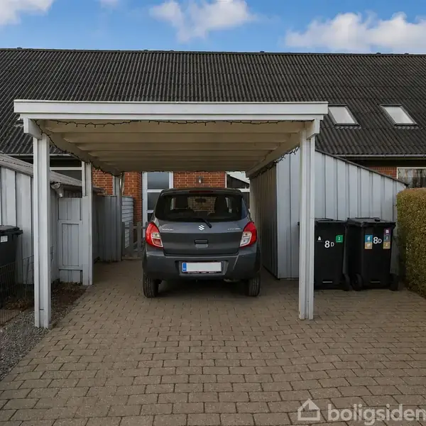 Køkken- og spiseområde med hvide skabe, spisebord med fire stole, og en fladskærm på væggen. Brune fliser på gulvet og træloft. Orkidé på lille træbord.
