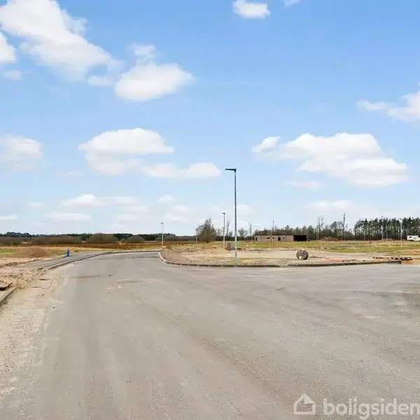 Vejsystem løber gennem et åbent, landskabeligt område, med asfaltveje og sparsomme træer i baggrunden under en skyet himmel.