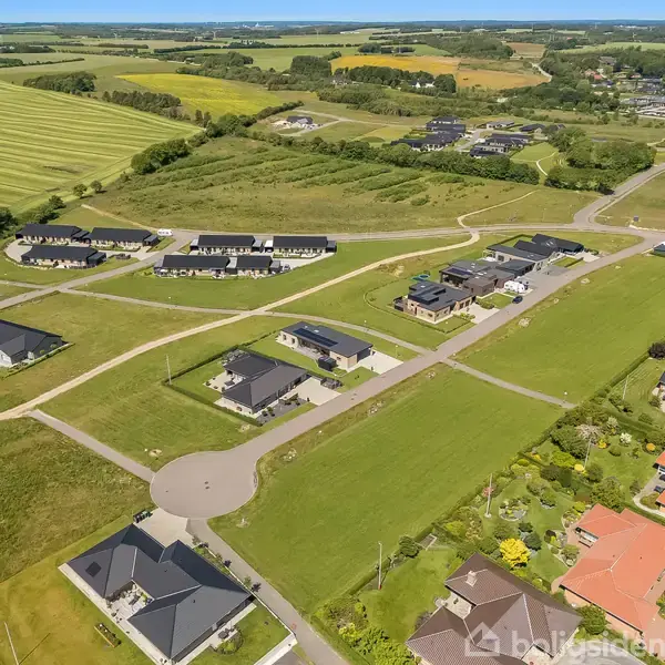 Et "Til salg"-skilt fra Nybolig står på en tom, jordet grund i et boligområde med huse og buske i baggrunden. Telefonnummer: 96 752 286.