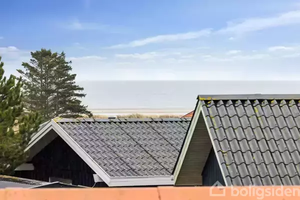 Rødt murstenshus med blå døre står i en have med græsplæne. Til venstre ses skraldespande, til højre en carport. Himlen er klar, omgivet af buske og træer.