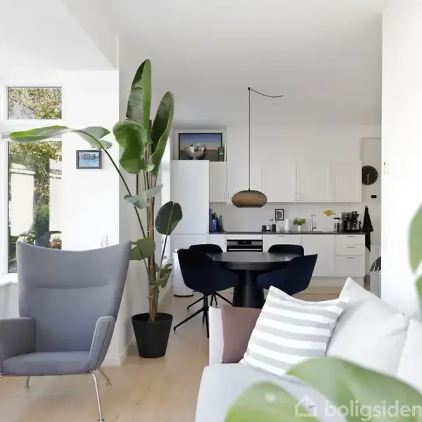 En moderne stue med grå lænestol og sofa, grønne planter på gulvet og væggen. Køkken med hvidt interiør i baggrunden. Store vinduer giver naturligt lysindfald.