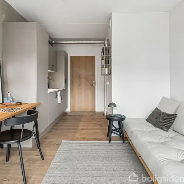 Et moderne køkken med en stor stålbordsplade og to indbyggede ovne i hvide skabe. Store vinduer giver udsigt til en moderne bygning og grøn vegetation udenfor.