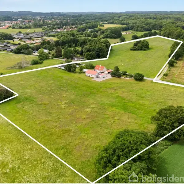 En stor grøn mark med et enkelt hus i centrum, omkranset af hvide grænselinjer. Skove og marker udgør den omkringliggende natur.