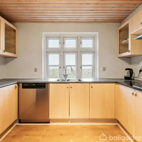 Køkken med lyse træskabe og skabsplads under en sort bordplade, hvor en vask med armatur er centralt placeret foran et vindue. En opvaskemaskine og kaffemaskine står til venstre.