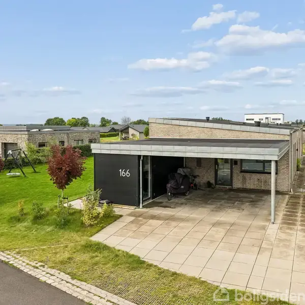 Et moderne parcelhus med fladt tag står stille i et grønt villakvarter. Huset har nummeret "166" på væggen, og der er en carport med en motorcykel under.
