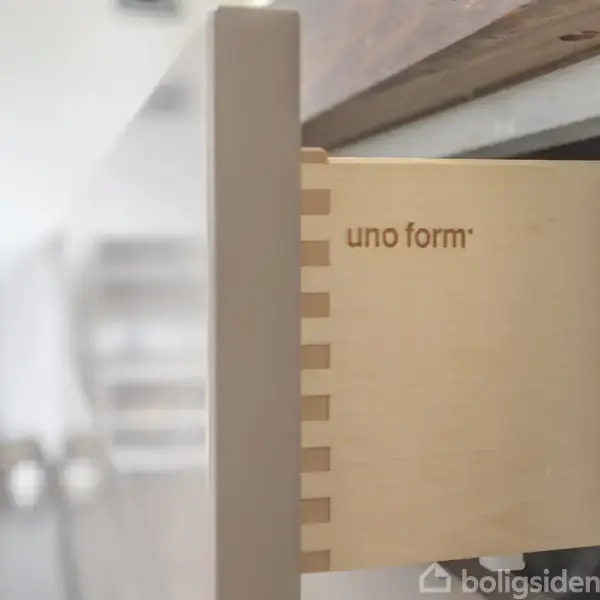 En åben skuffe med teksten "uno form" ses i et moderne køkkenmiljø. Skuffen er delvist trukket ud, hvilket viser dets lyse træindvendige design.