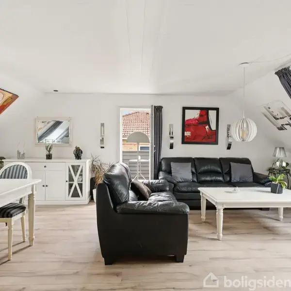 Stue med sort lædersofa og sofabord, spisestue med hvidt bord og stole. Væggene har kunstværker, og rummet er lyst med skråvinduer. Tæpper og planter i hjørnet.