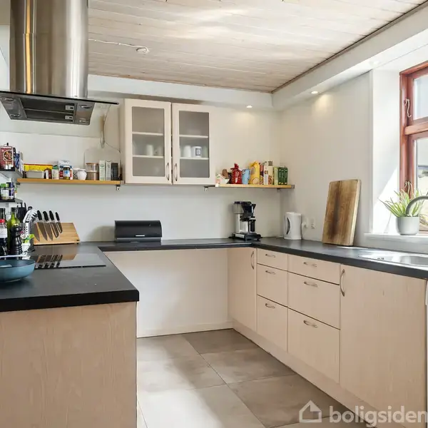 Et moderne køkken med sort bordplade, indrettet med skabe, hylder med køkkenartikler, og en stor vask under et vindue. Der er også en emhætte og diverse køkkenredskaber på bordet.