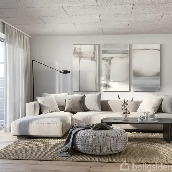 En lys stue med en stor, hvid sofa fyldt med puder. Foran sofaen står et rundt, gråt strikket puf og et fladt sofabord. På væggen hænger tre abstrakte malerier.