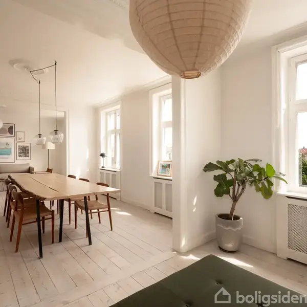 Spisebord omgivet af stole står i et lyst rum med hvide vægge og lyse trægulve. Store vinduer giver udsigt til en by, mens en grøn plante står i et hjørne.