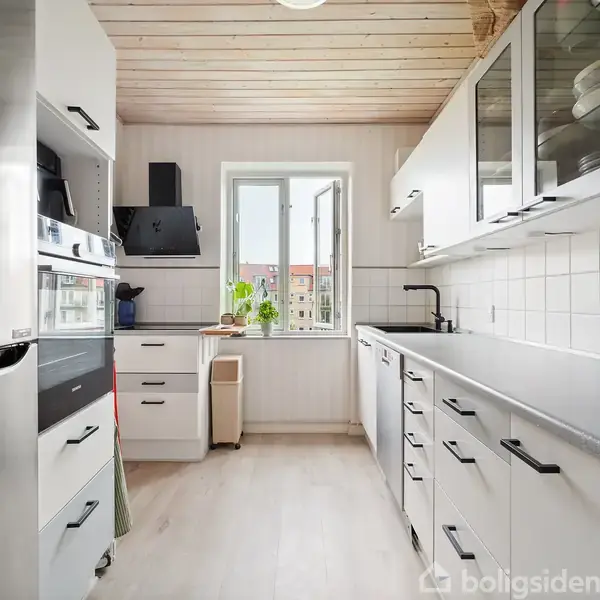 En lys stue med en grå sofa, et tv på stativ, vægkunst og et rundt spisebord med stole i træ. Plakater pryder væggen, og planter giver et grønt touch.