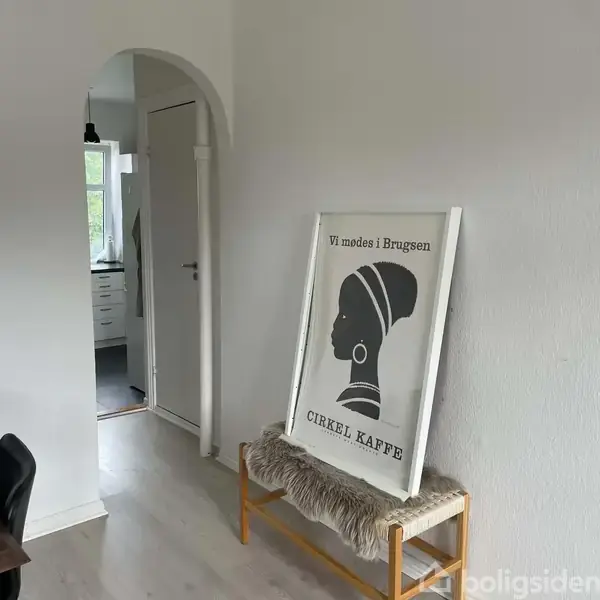 En plakat med silhuet af en kvindes hoved står op ad en væg. Teksten på plakaten lyder: "Vi mødes i Brugsen, Cirkle Kaffe". Den står i en lys gang.