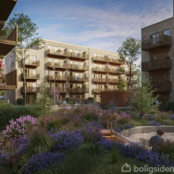 Flere boligblokke omkranser en grøn gård med farverige blomsterbede og en sandkasse, hvor en person sidder. Bygningerne har altaner, og træer giver skygge til området.