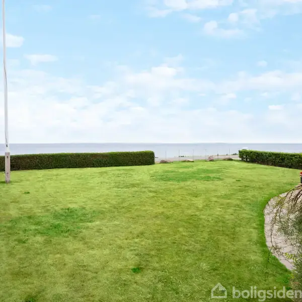 Badeværelse med hvidt badekar, bruser med forhæng, og lang vaskebord med spejl. En blå skål står på bordet. Flisegulv og hvidmalede vægge skaber et moderne udtryk.