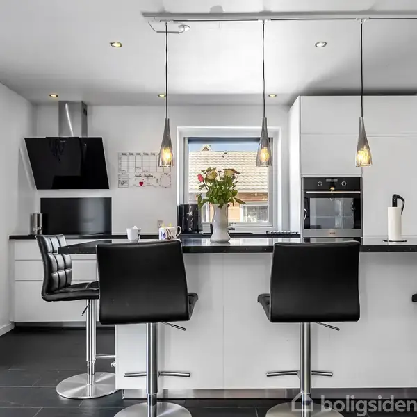 Moderne køkken med barstole står ved en sort-hvid køkkenø. Tre hængelamper lyser rummet op. Tekst på væggen: "Life is like a camera. Capture the good times. Develop from the negatives. And if things don't work out, take another shot."