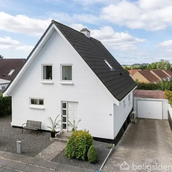 Hvidt hus med sort tag står stille i et boligområde. Forhaven har en bænk, en lille busk, og en flisebelagt sti. Nummer 55 vises ved indgangen.