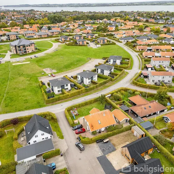 Beboelsesområde med moderne huse, nogle med flade tage, andre med skrå, omkranser store grønne områder og stier i en landsbylignende struktur. Boligerne er arrangeret langs buede veje.