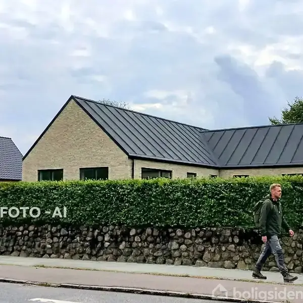 En mand går langs en vej foran en moderne villa med fladt tag og murstensfacade. Villaen er omgivet af en høj hæk og en stensætning. Tekst: "MODELFOTo - AI".