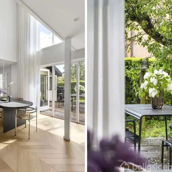 Spisebord med blomster og stole i elegant, lys spisestue. Stort vindue åbner ud til terrasse med bord og stole, omgivet af frodige grønne planter.