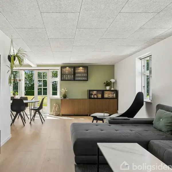 Spisebord med sorte stole i en spisestue. Glassdøre står åbne mod en grøn have. Væggen til venstre har en guitar og en barvogn ved siden af et vindue.