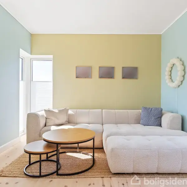 En hvid hjørnesofa står i en lys stue med blå og grønne vægge. Runde sofaborde er placeret foran sofaen. Væggene har moderne kunst og dekorative elementer.