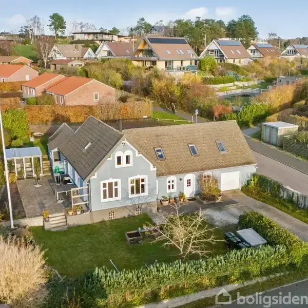 Et blågråt hus med en velholdt have og parkeringsplads i en forstadskvarter. Omgivet af lignende huse, grønne buske og små veje i et fredeligt nabolag.