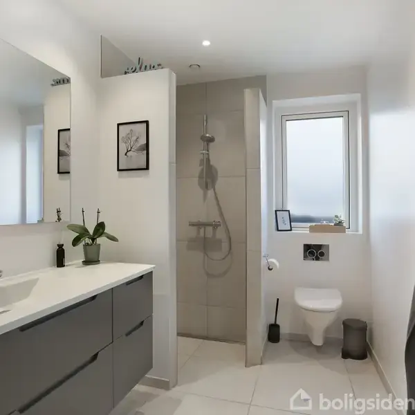 Badeværelse med dobbelt håndvask på grå skabsenhed, bruser i åben kabine, og toilet nær vindue. Der hænger håndklæde på krog, og planter samt billeder dekorerer rummet.