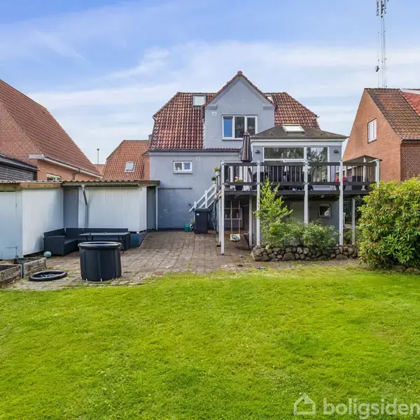 Huset har en tagterrasse med trappe, omgivet af grøn have og flisebelagt gårdhave. Der er en udendørs jacuzzi ved siden af en mindre træterrasse.