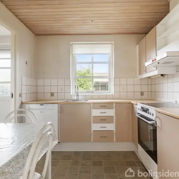 Et køkken med beige skabe og en ovn, der sidder i en bordplade ved siden af en vask. Der er flisevægge og et vindue, der viser en have udenfor.