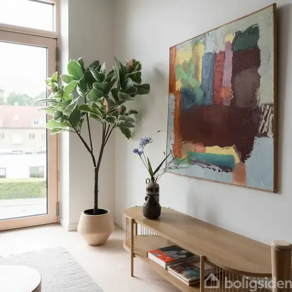 Et moderne stueområde med en stor, farverig abstrakt maleri på væggen, en grøn plante i potte til venstre og et træbord med bøger og en vase foran et vindue.