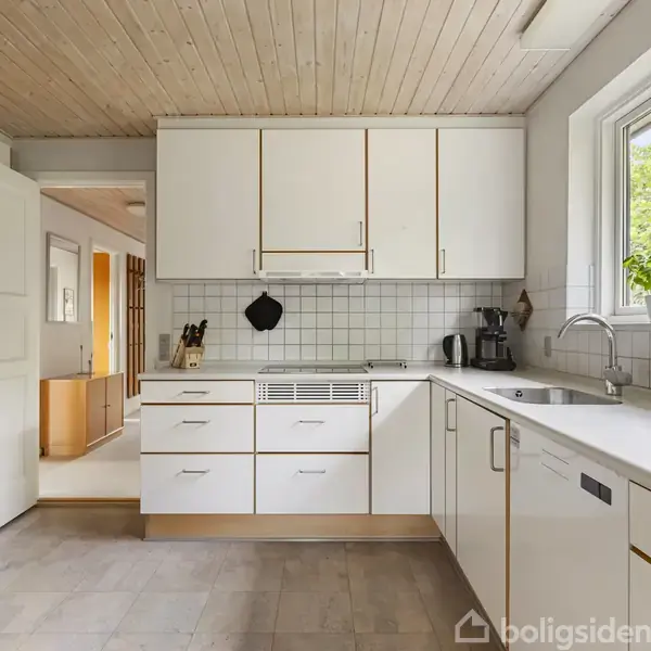 Et gult murstenshus står i en stor, tør have med græs og buske; parasol ved terrassen. Omkringliggende træer og naboens huse skaber en rolig forstadskontekst.