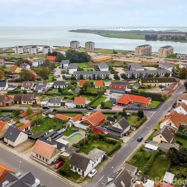 Boligkvarter med huse med røde tage ligger nær kysten. Baggrund viser vandet og en bro i horisonten. Området er omgivet af både bygninger og grønne områder.
