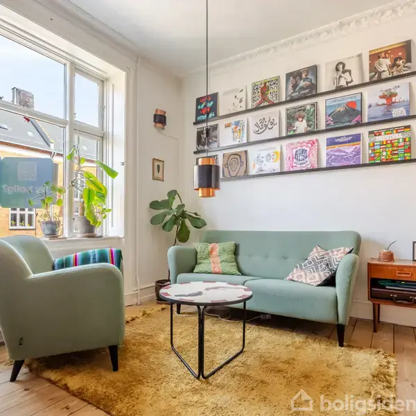 En stue med en mintgrøn sofa og lænestol. En væg prydes af albumcovers. Et gulvtæppe ligger på trægulvet, ved siden af et vindue og en lampe. En pladespiller står i hjørnet.