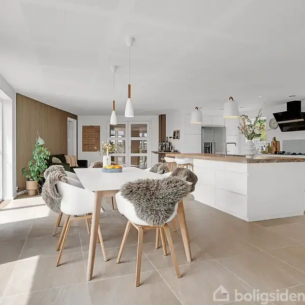 Et moderne køkken-alrum med en rund spisebord omgivet af stole beklædt med pels. Køkkenøen har hængende lamper. Store vinduer til venstre giver naturligt lys.