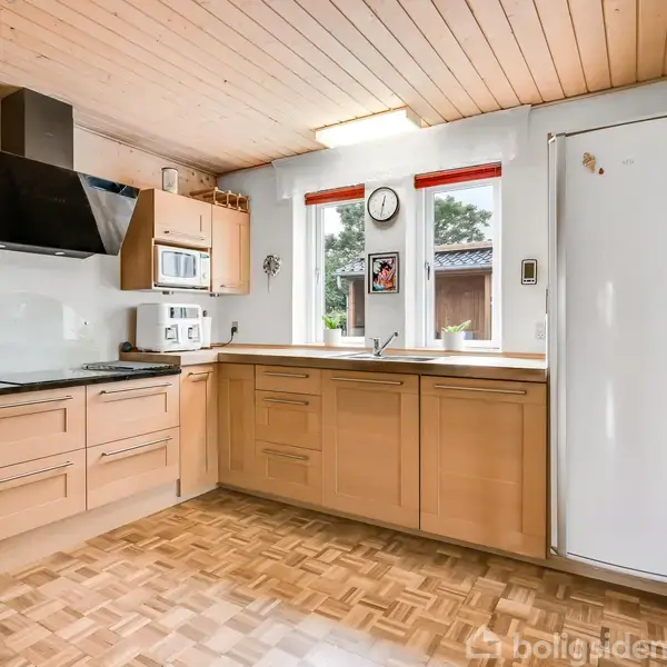 Køkken med træskabe og træloft, inkluderer en stor hvid køleskab, indbygget ovn, mikroovn og kogeplade. To vinduer med røde persienner giver udsigt til en have.