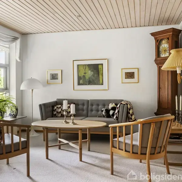 En stue med en grå sofa og to træstole centreret omkring et ovalt sofabord. Omgivet af billeder på væggene og en stor standerlampe ved vinduet.