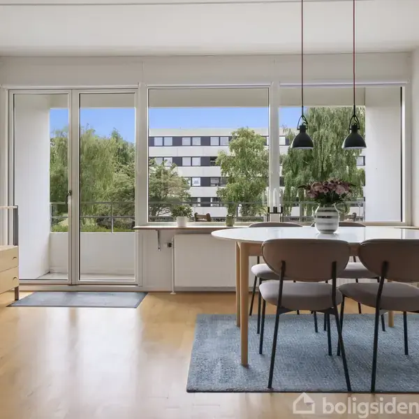 Et spisebord med fire stole står på et blåt tæppe, omgivet af lyse træmøbler og en reol. Store vinduer åbenbarer en udsigt til grønne træer og boligblokke udenfor.