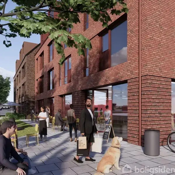En mand går med en indkøbspose foran en moderne murstensbygning. Et skilt står ved indgangen. Mennesker sidder og står på fortovet, mens cykler og træer er i nærheden.